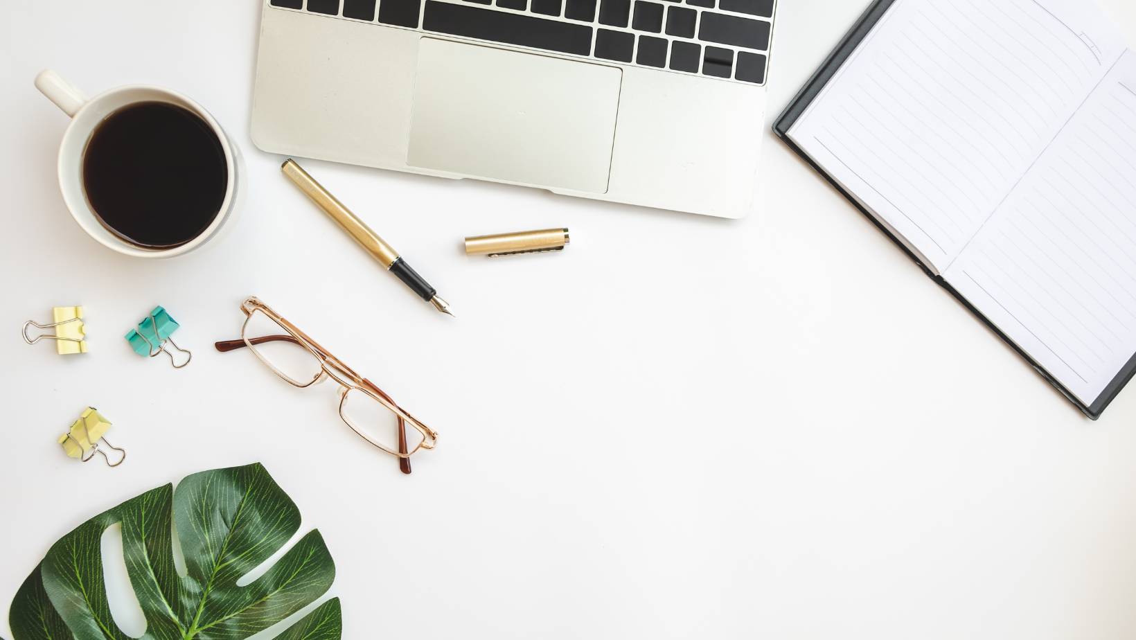overhead view of a desk with glasses, notebook, pen, plant